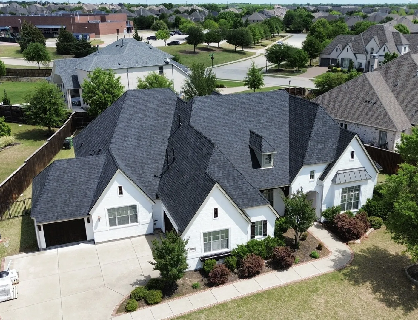The completed roof in dark architectural shingle on a white brick home, seen from above