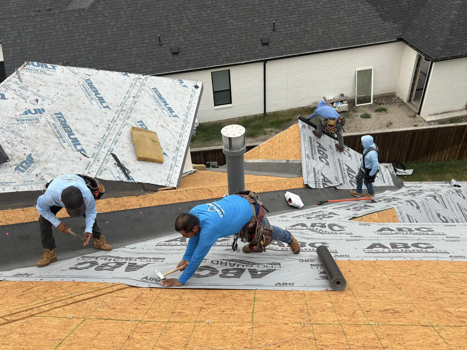 TopLine crew rolling synthetic underlayment across fresh decking on a Dallas-area roof